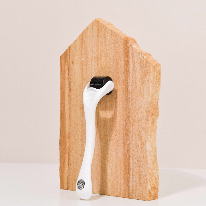 Wildcrafted Organics Microneedle Dermal Roller liegt lehnt an einer Steinplatte.