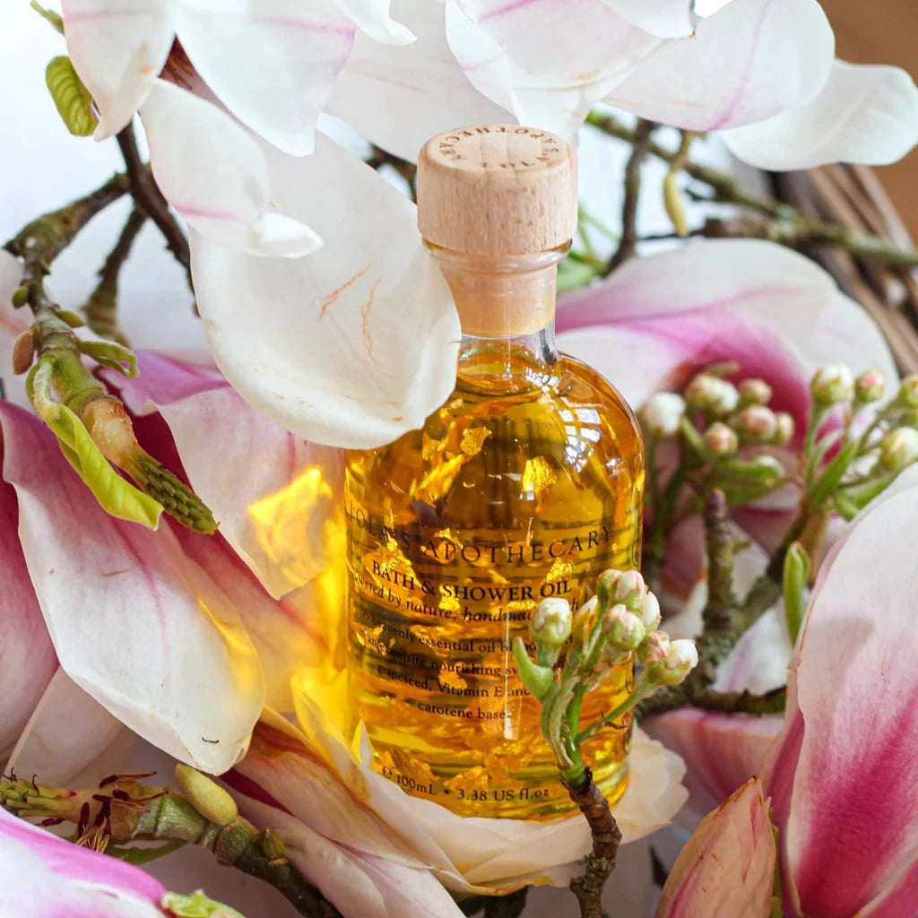 Eine Glasflasche Bath & Shower Oil von Lola's, steht zwischen Orchideenblüten.