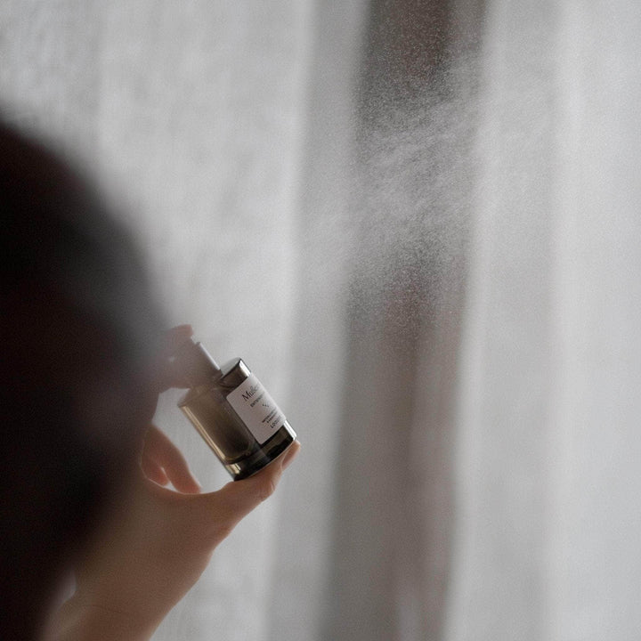 Eine Hand sprüht ein Raum- und Kissenspray in die Luft.