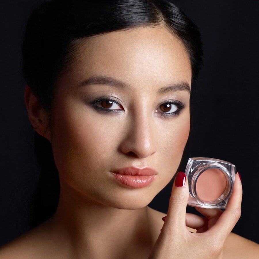 Eine Frau hält den Powder Blush MELISENDE von Le Rouge Francais in einer Hand neben ihr Gesicht.