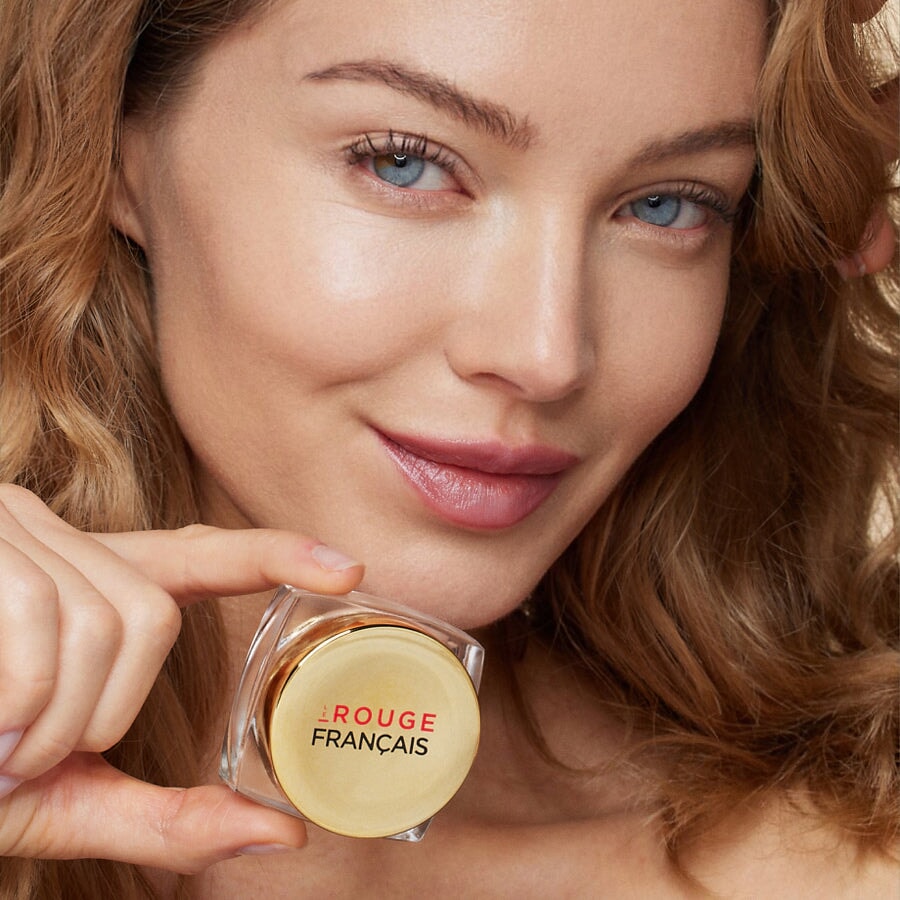 Eine Frau hält AÏTUTAKI von Le Rouge Francais unter ihr Gesicht.