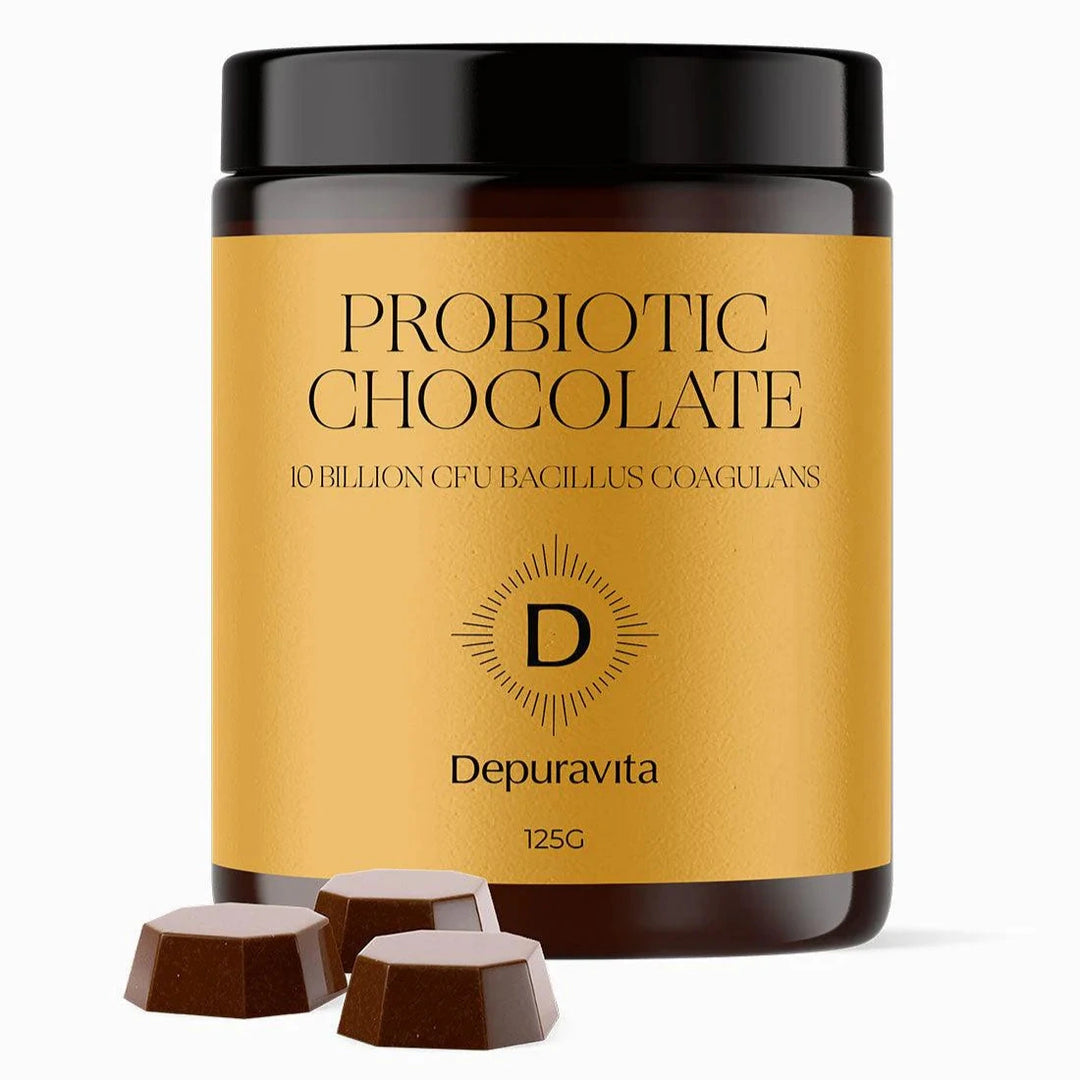 Braunes Glasgefäß mit gelbem Etikett PROBIOTIC CHOCOLATE von Depuravita, daneben drei Schokoladenstücke.