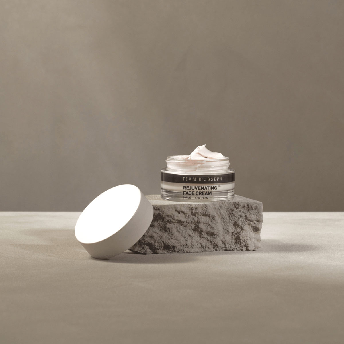 Offener Cremetiegel der Rejuvenating Face Cream von Team Dr Joseph auf grauer Steinplatte, luxuriöse Anti-Aging-Creme mit glatter, weißer Textur.