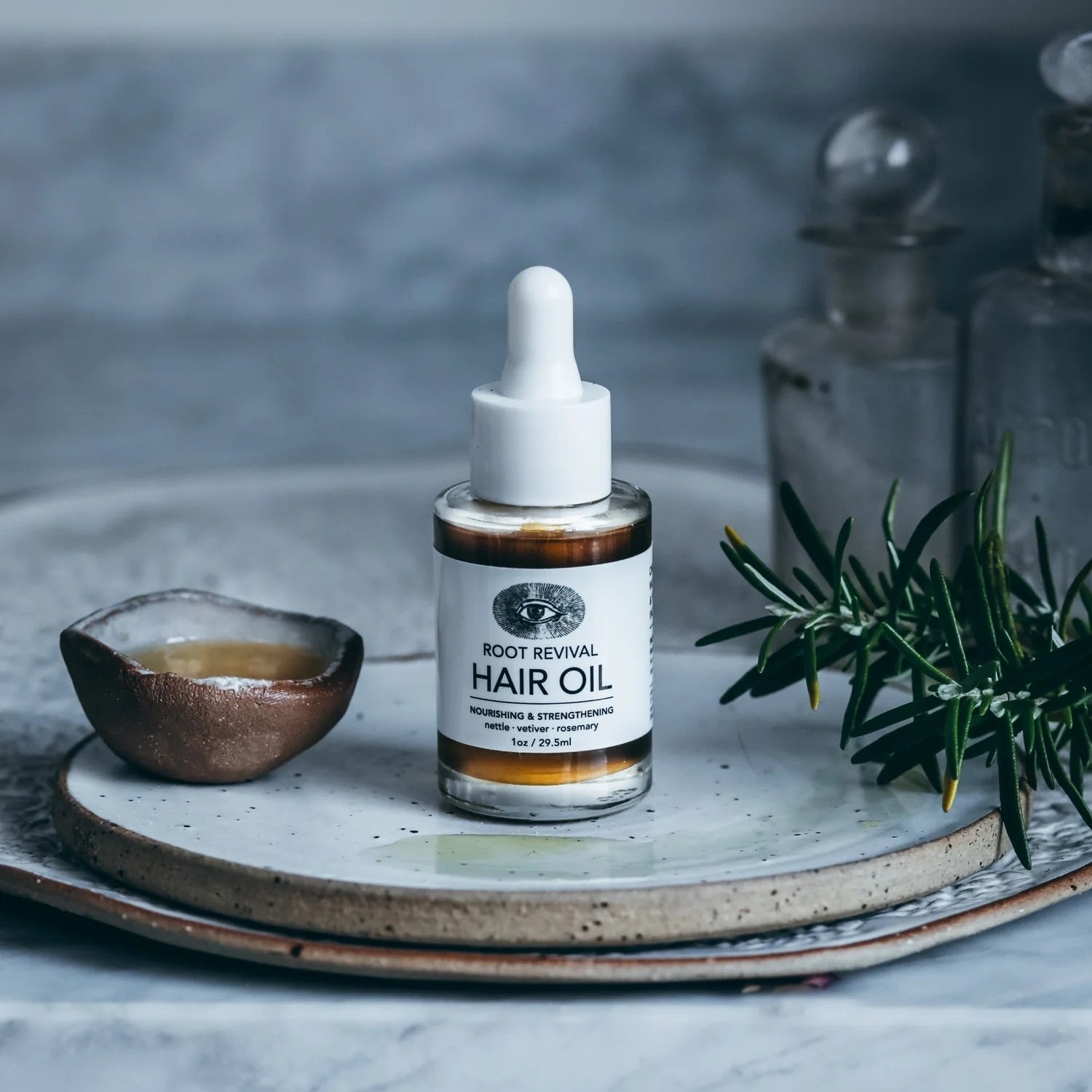 Pipettenflasche Anima Mundi Hair Oil steht neben einem Schälchen mit Öl gefüllt.