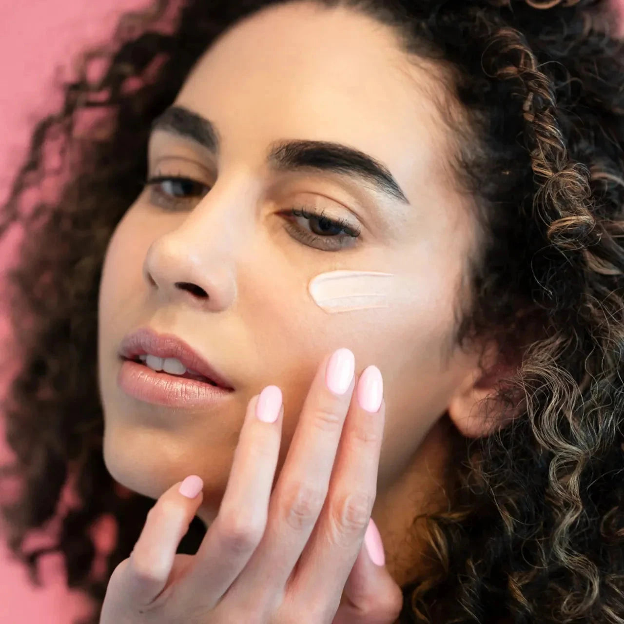  Rose Rejuvenating Face Cream Textur auf dem Gesicht einer Frau mit dunklen Locken