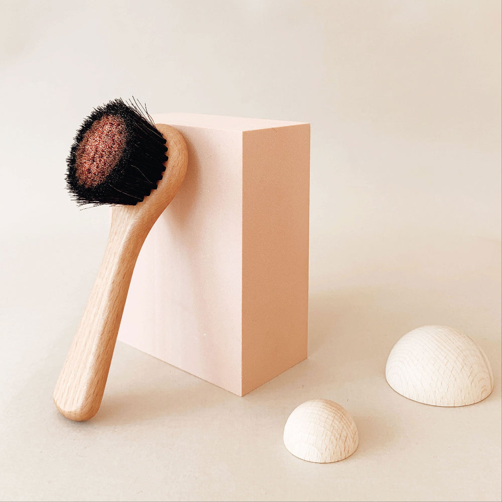 Minimalistisches Studio-Arrangement: Die ruhi Gesichtstrockenbürste lehnt an einem pastellrosa Block neben weißen, runden Deko-Elementen.