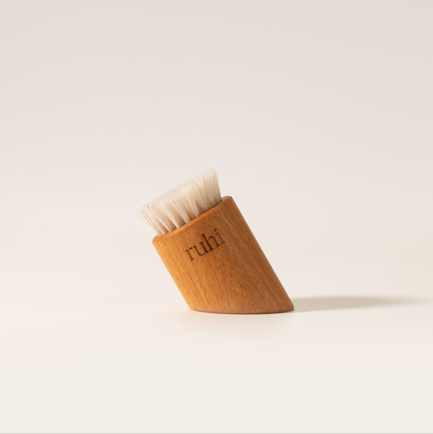 Die ruhi Vegan Facial Dry Brush, eine schräg geschnittene Gesichtstrockenbürste aus Holz mit hellen Borsten.