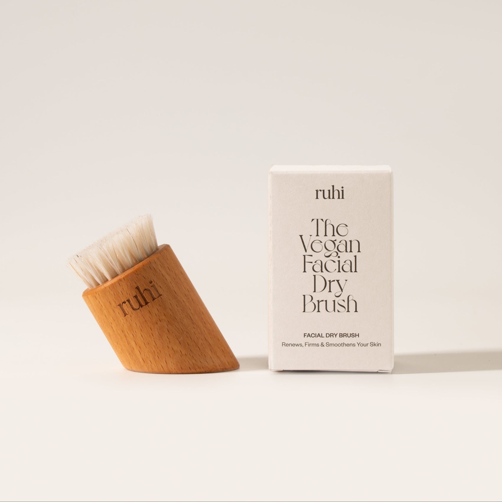 Die vegane Gesichtstrockenbürste von ruhi neben ihrer minimalistischen weißen Produktverpackung.