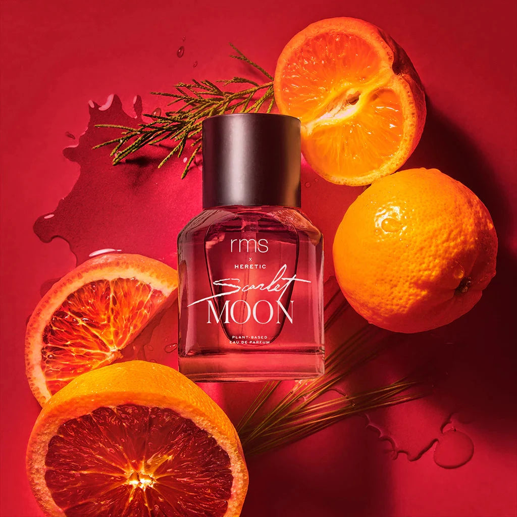 Rote RMS und X Heretic Scarlet Moon Parfum Flasche mit schwarzem Deckel auf rotem Hintergrund liegt zwischen Orangen und Blutorangen.