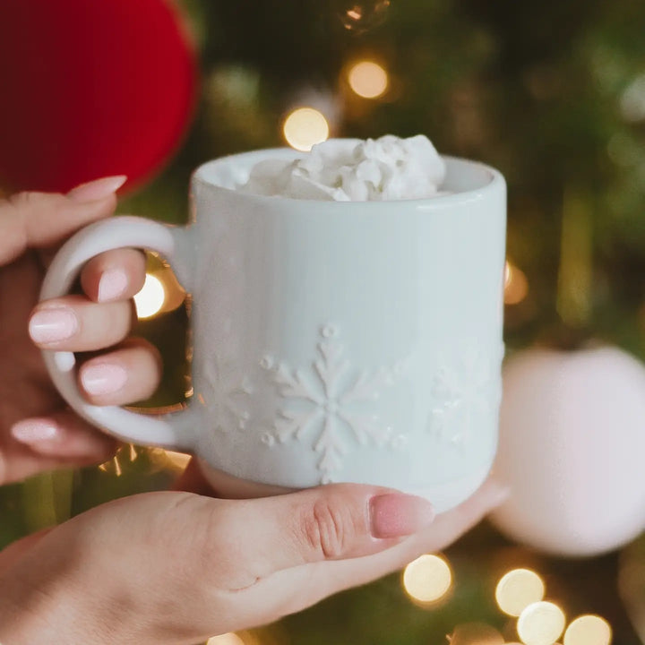 Wintertasse mit Schneeflocken-Motiv aus Keramik, in beiden Händen gehalten