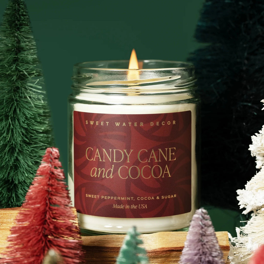 Brennende Duftkerze Candy Cane and Cocoa im Glas steht zwischen kleinen Deko-Weihnachtsbäumen. North Glow