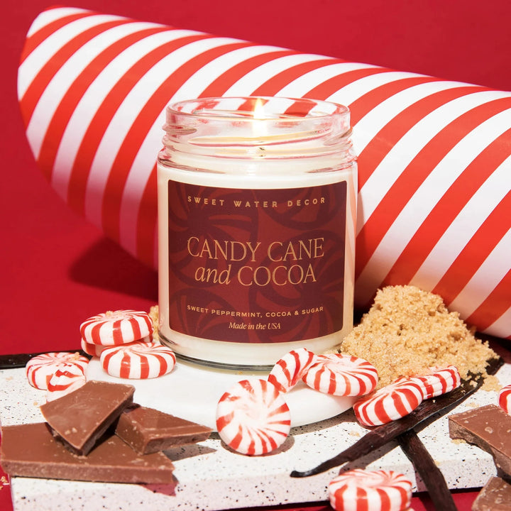 Duftkerze Candy Cane and Cocoa im Glas steht zwischen Zucker, Bonbons und Stückchen Schokolade.