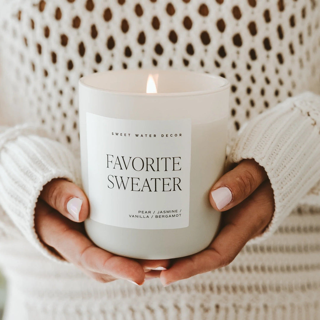 Zwei Hände halten die Duftkerze Favorite Sweater von Sweet Water Decor vor dem Körper.