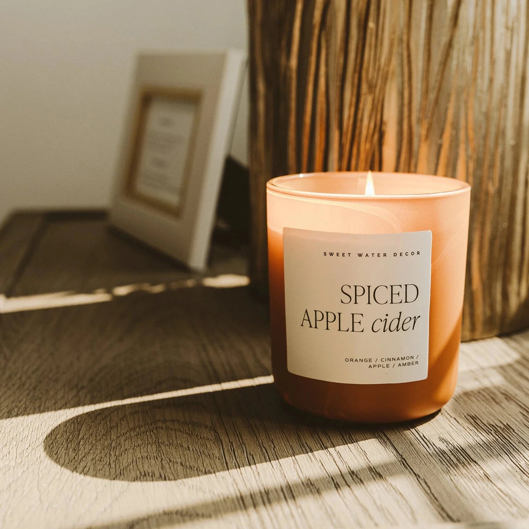 Brennende Spiced Apple Rider Sojawachskerze von Sweet Water Decor auf Holztisch, angestrahlt von der Herbstsonne