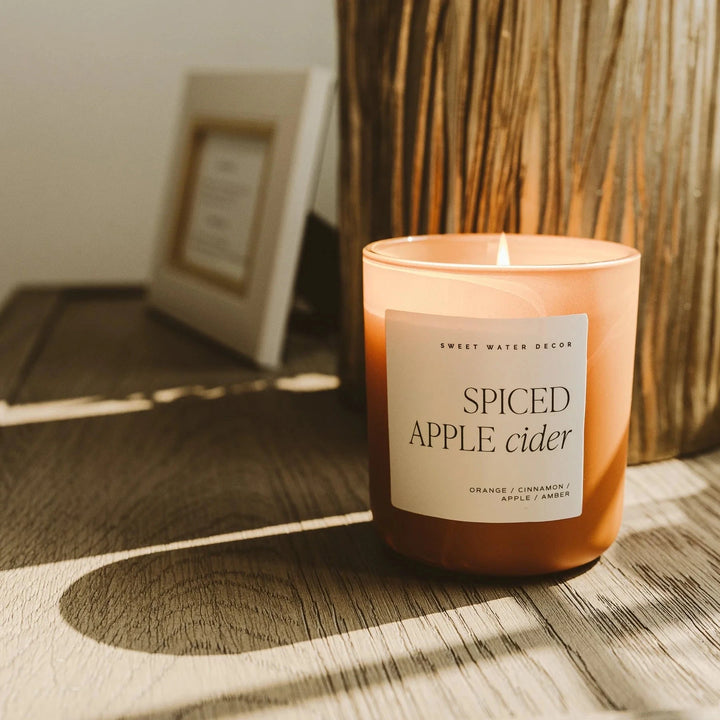 Brennende Spiced Apple Rider Sojawachskerze von Sweet Water Decor auf Holztisch, angestrahlt von der Herbstsonne