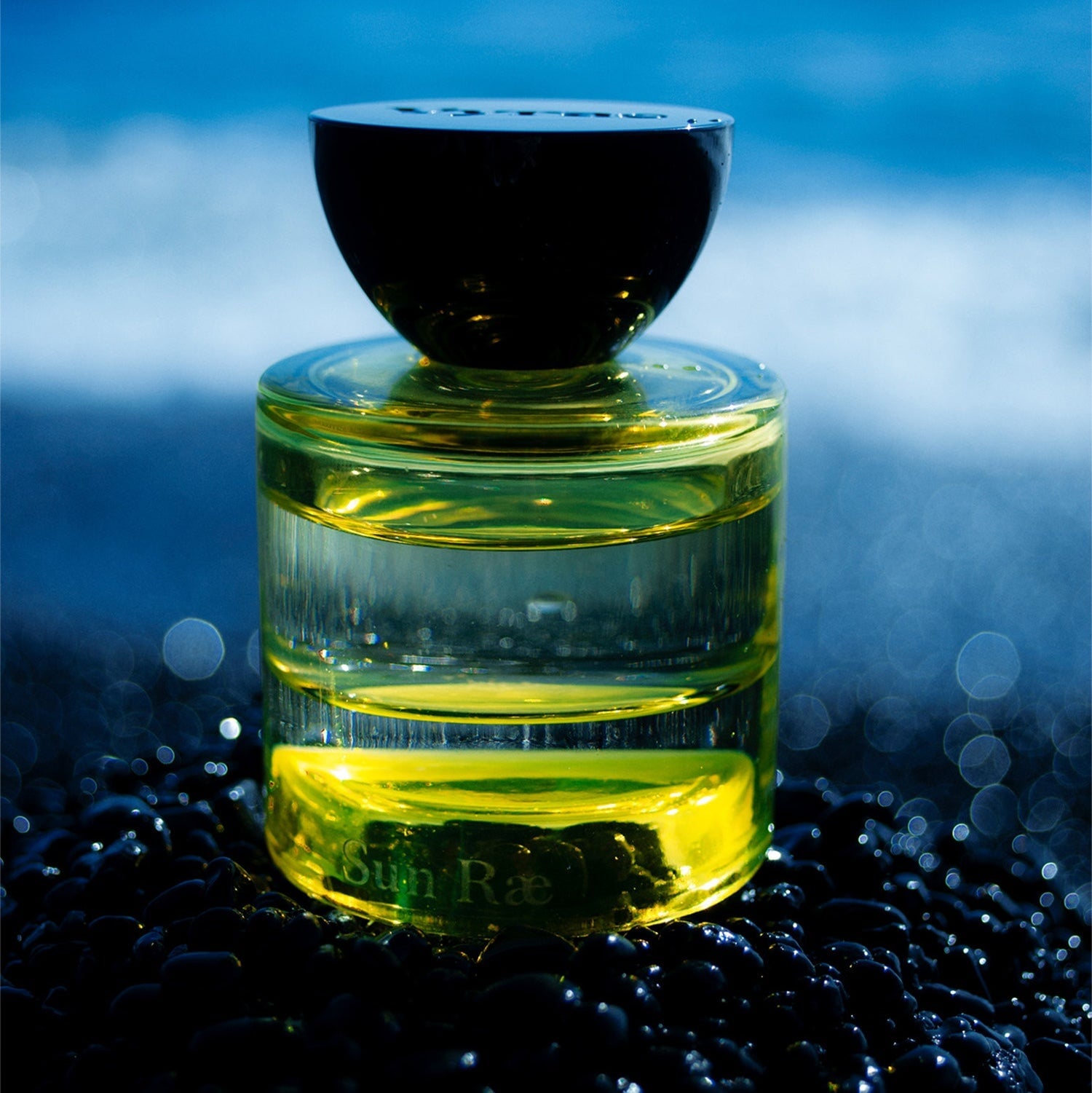 Gelber Glasflakon mit schwarzem Deckel Vyrao Sun Rea steht vor abendlichen Hintergrund.