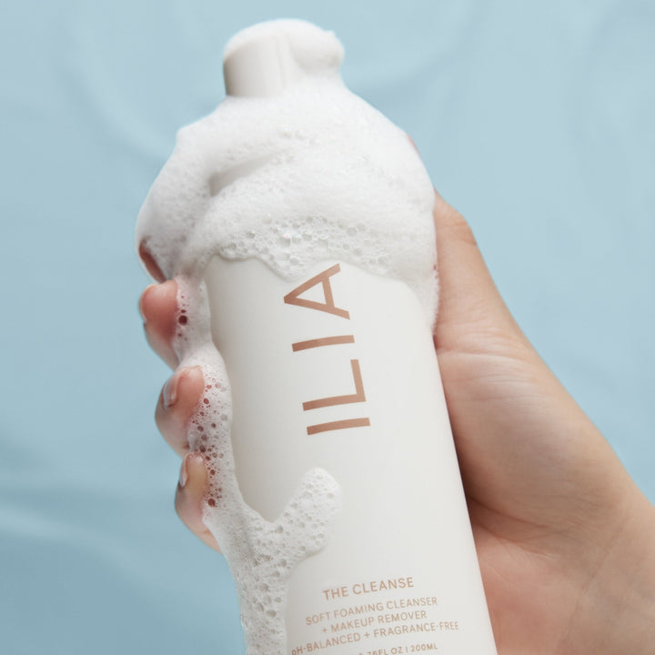 Eine Hand hält eine  ILIA The Cleanse Pumpflasche an der Schaum herunterläuft.