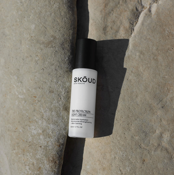 SKŌUD The Protection Light Cream Pumpflasche mit schwarzem Deckel  liegt in einer Felsspalte.