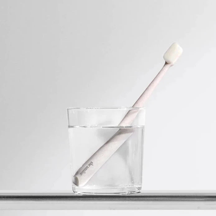 Rosafarbene the smilist Zahnbürste steht in einem mit Wasser gefülltem Glas vor hellem Hintergrund.