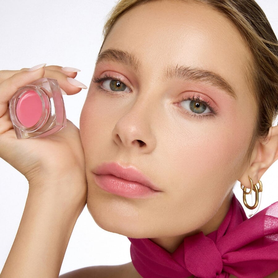 Eine Frau hält den Lippenbalm DAVIA von Le Rouge Francais in der Hand neben ihr Gesicht. North Glow