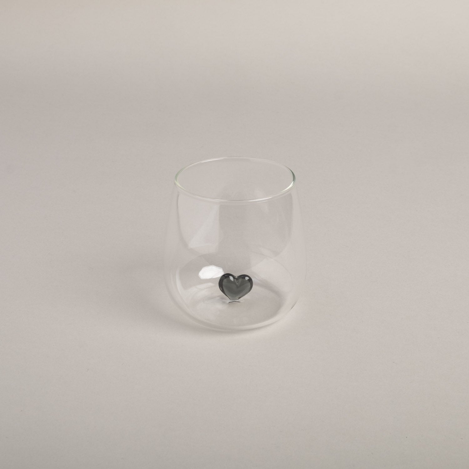 Bauchiges Trinkglas mit schwarzem Herz im Zentrum von Eulenschnitt steht vor hellem Hintergrund.