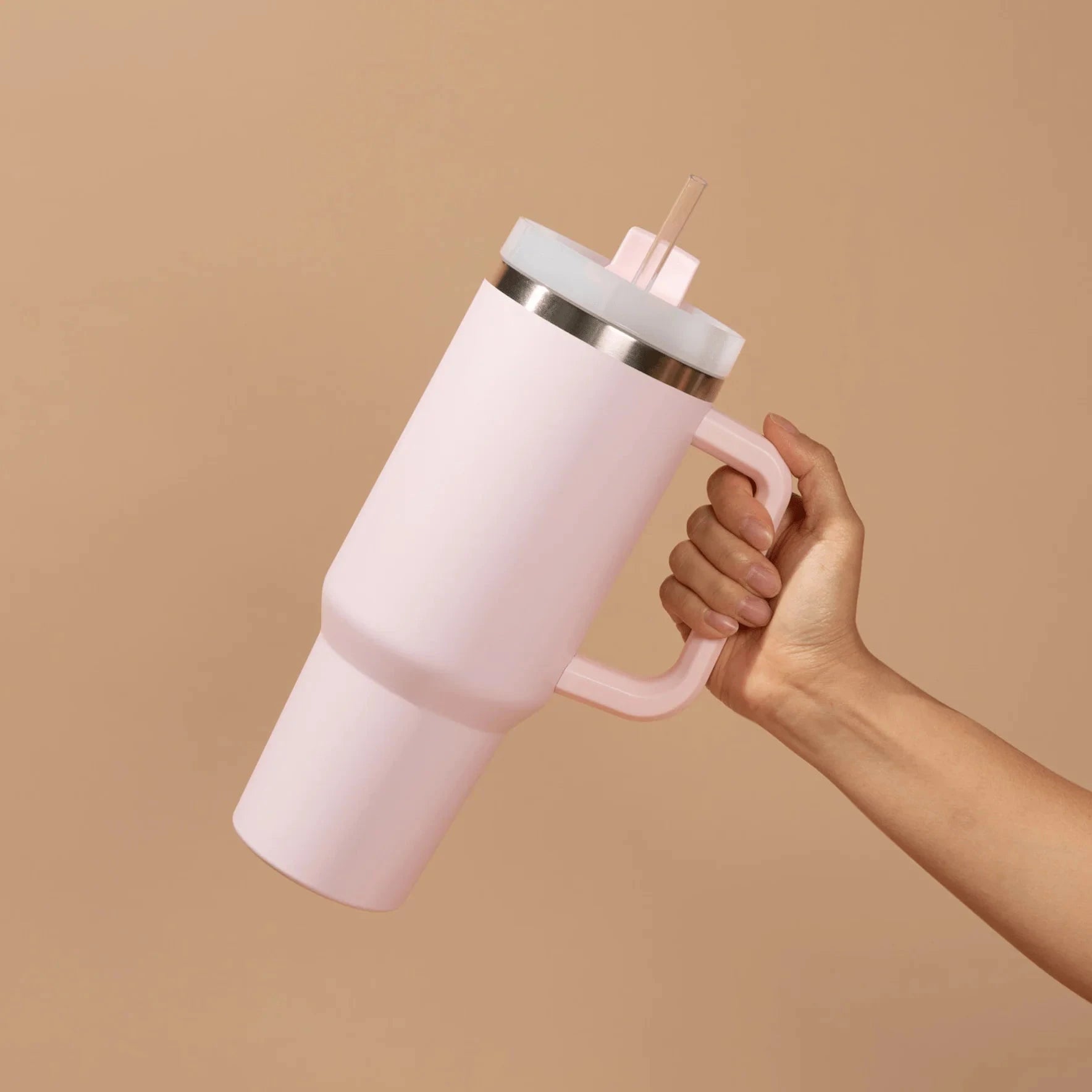 Eine Hand hält einen rosafarbenen Tumbler / Thermobecher von Sweet Water Decor vor hellem Hintergrund.