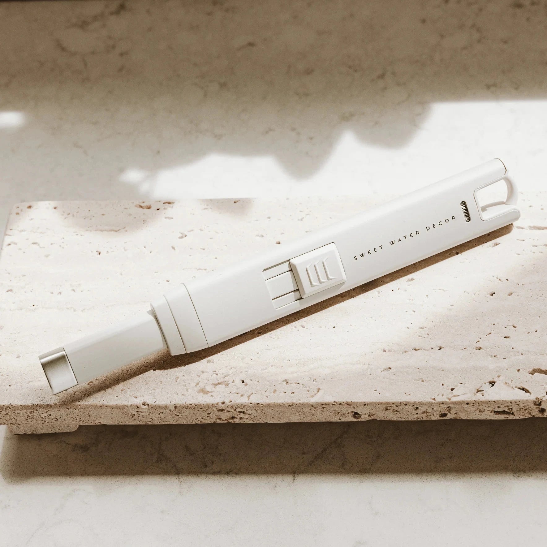 Weißes USB rechargable Feuerzeuge SWEET WATER DECOR liegt auf einer Steinplatte.