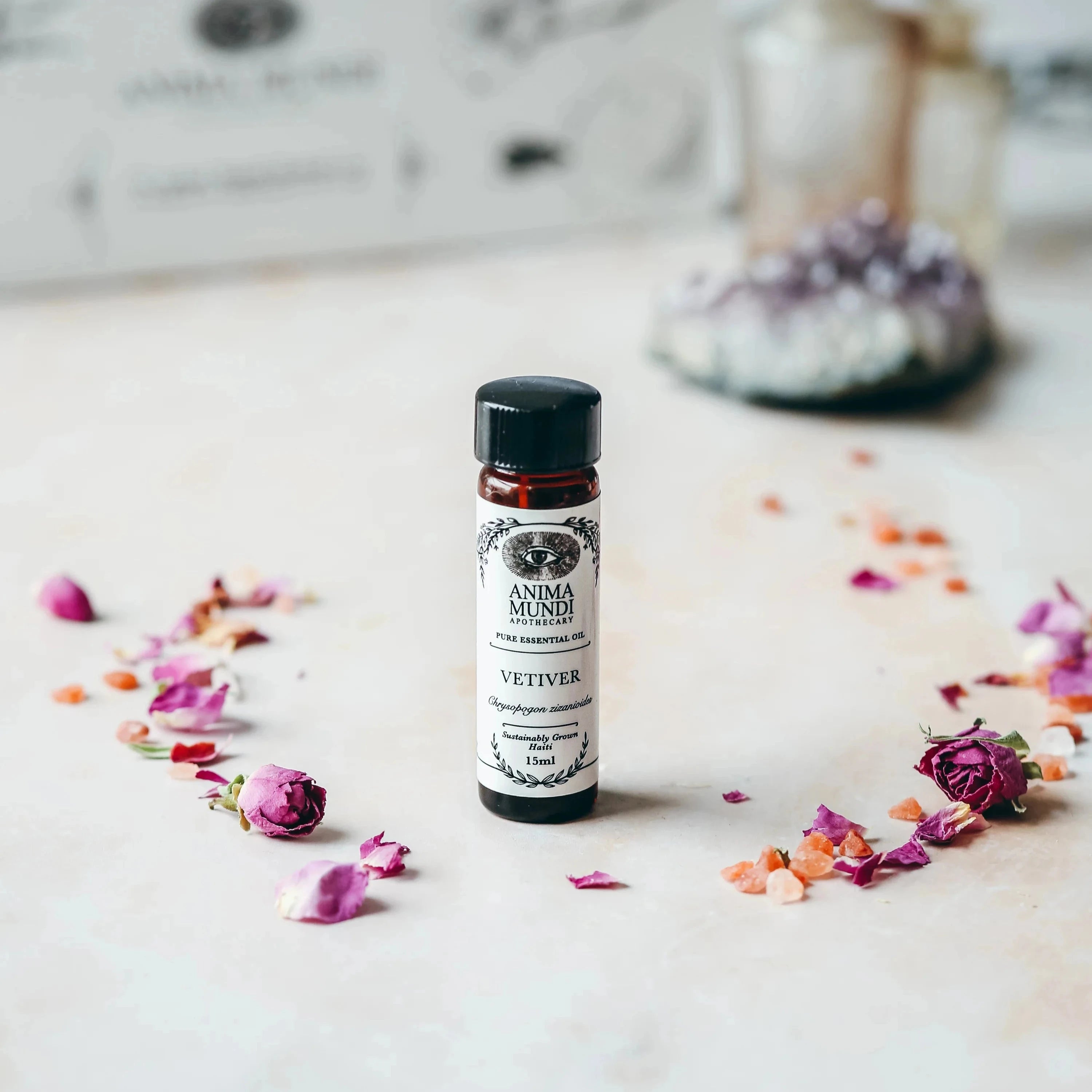 Vetiver Essential Oil von Anima Mundi stehend, umgeben von Blütenblättern.