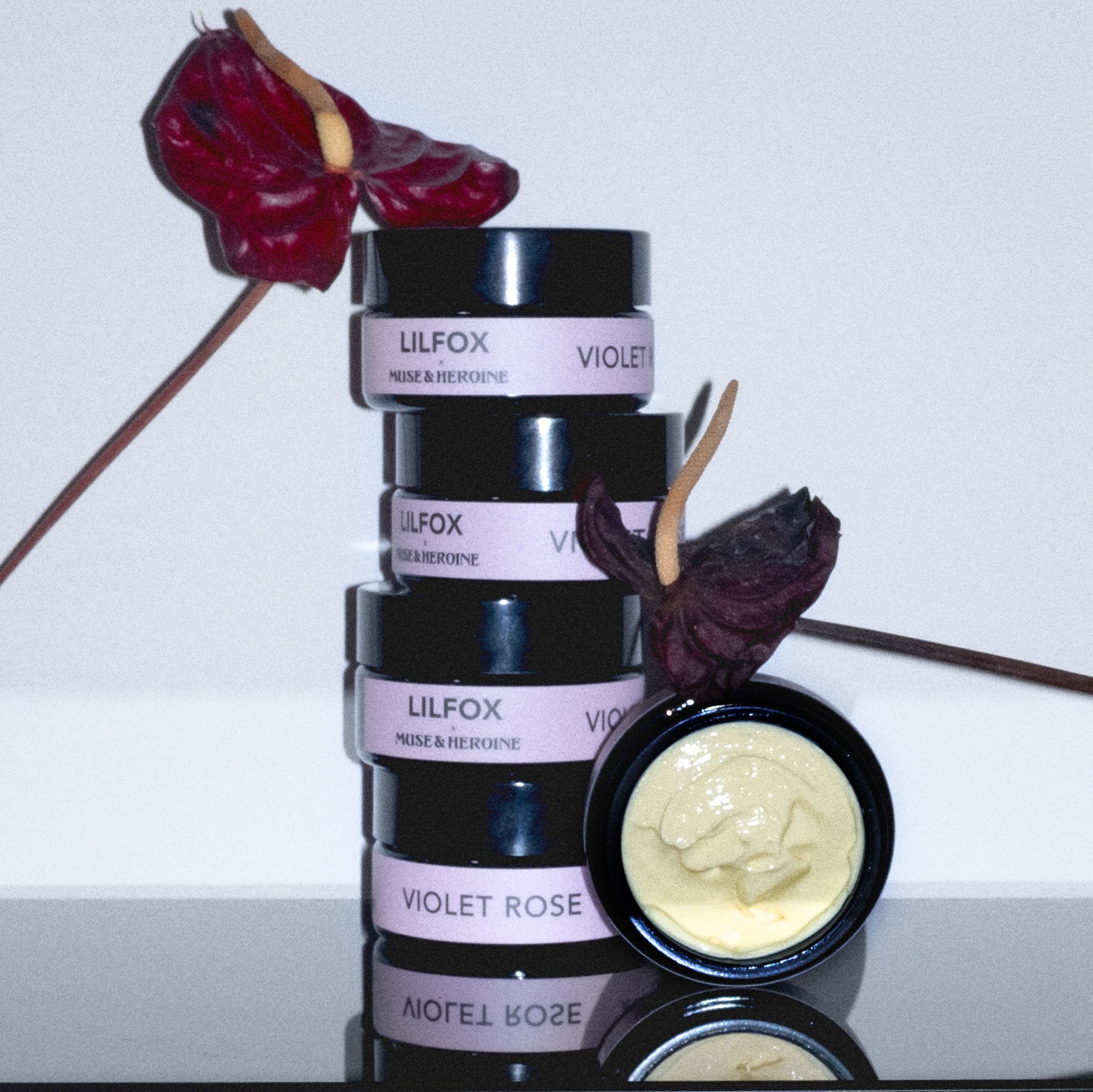 Lilfox Violet Rose Tiegel aufeinander gestapelt  Ein Tiegel offen Links und rechts rote Blumen mit langem Nippel  Hellblauer Hintergrund