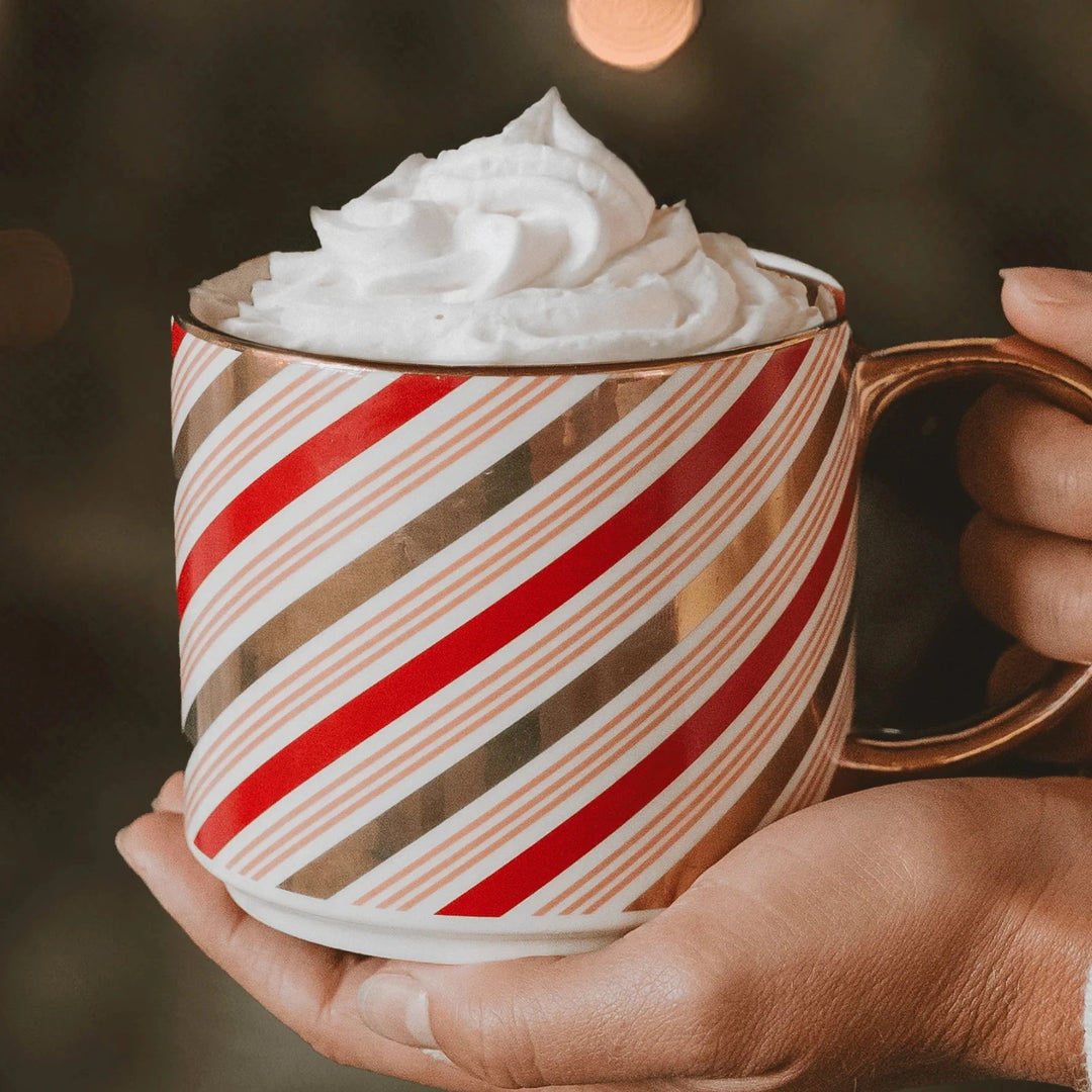 Sweet Water Decor Tasse Candy Cane mit Sahnehaube, wird von 2 Händen gehalten.