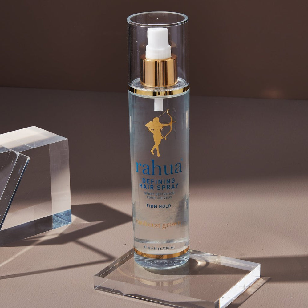 Rahua Defining Hair Spray Flasche steht auf Plexiglasscheibe vor braunem Hintergrund.