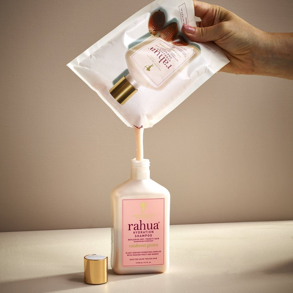 Hand hält Rahua Hydration Shampoo Refillpouch in der Hand und füllt Inhalt in die Flasche um.