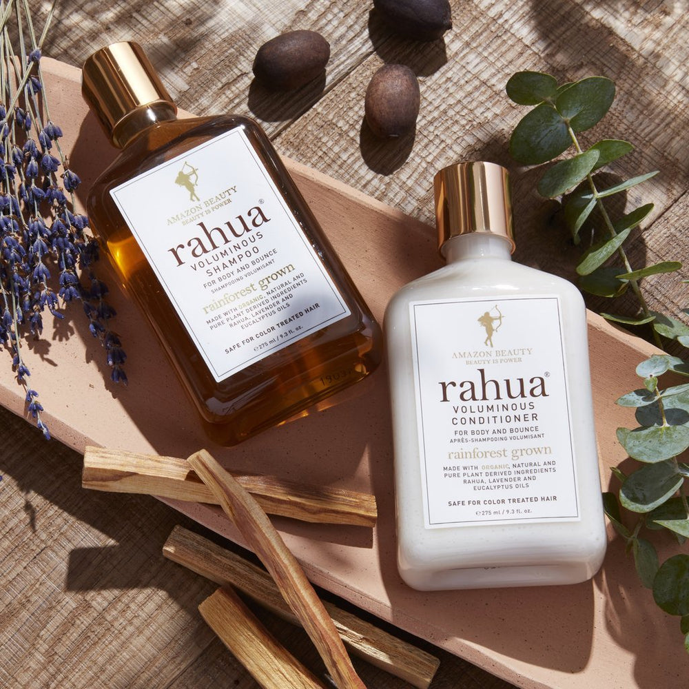 2 Rahua Flaschen Voluminous Shampoo und Conditioner in Nahaufnahme liegen auf einem Tisch mit Rahuanuss, Eukalyptus und Lavendel.