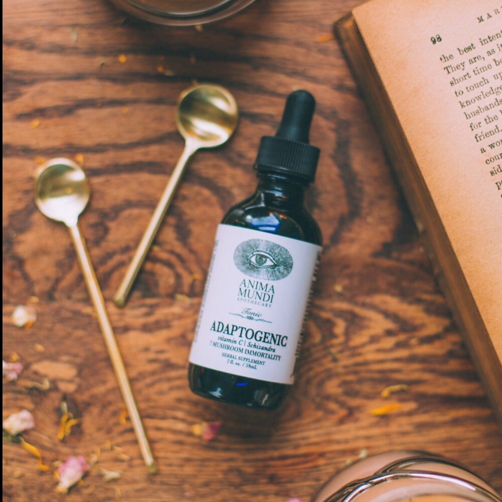 Anima Mundi Glasflasche Adaptogenic, liegt auf einem Holztisch neben 2 Messinglöffeln.