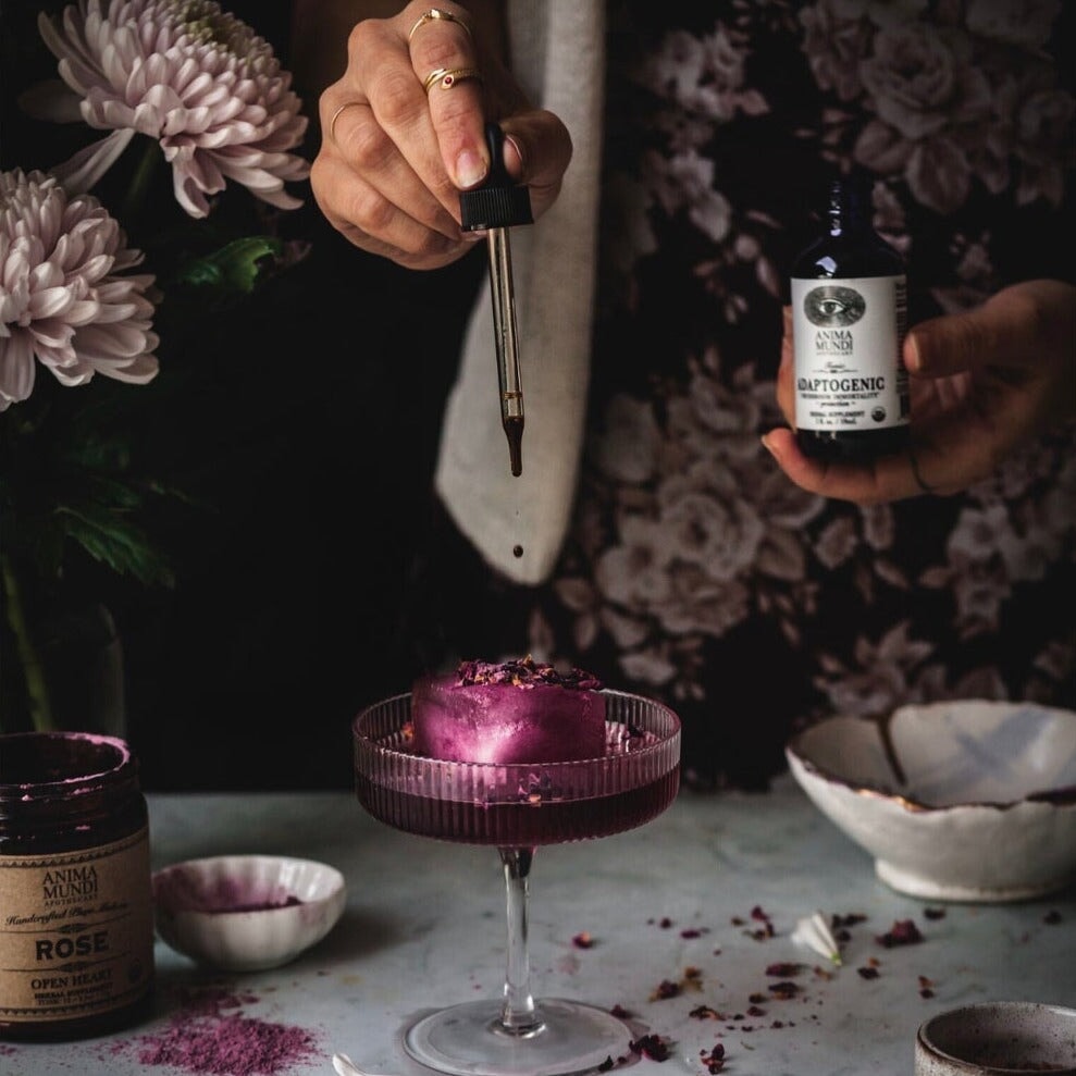 Eine Hand hält eine Anima Mundi Glasflasche Adaptogenic, die andere hält eine Pipette über ein Dessert Glas.