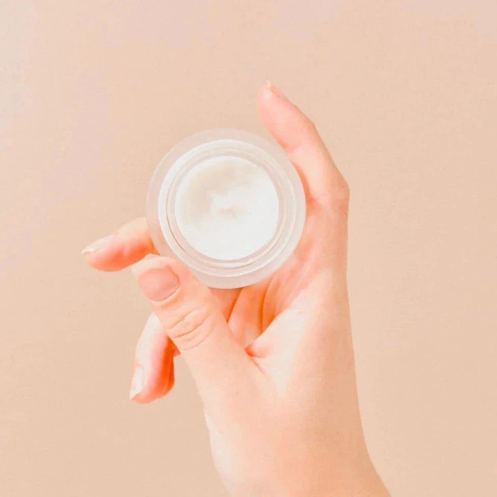 Eine Hand hält einen offenen Milchglastiegel Wildcrafted Bioactive Eye Serum. North Glow