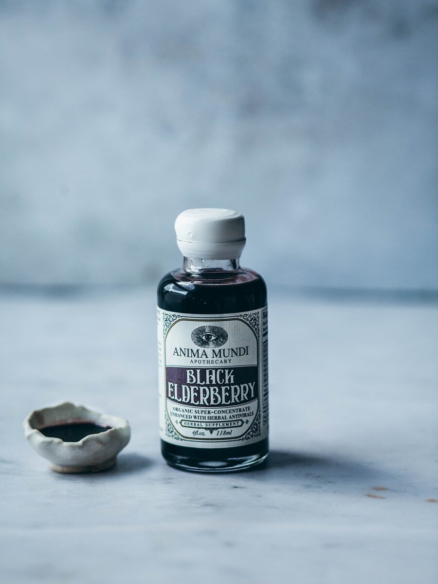 Anima Mundi Glasflasche Black Elderberry steht neben einer kleinen Steingutschale gefüllt mit Holunderbeersirup.