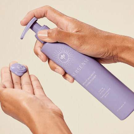 Hand hält eine Innersense Bright Balance Conditioner Flasche und pumpt Conditioner in die andere Hand.
