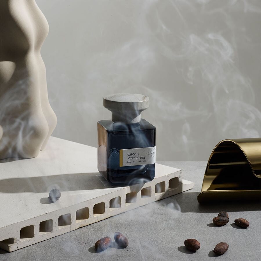 Dunkelblaue Glasflasche mit grauem Deckel "Cacao Porcelana" von Atelier Materi umgeben von leichtem weißem Rauch.