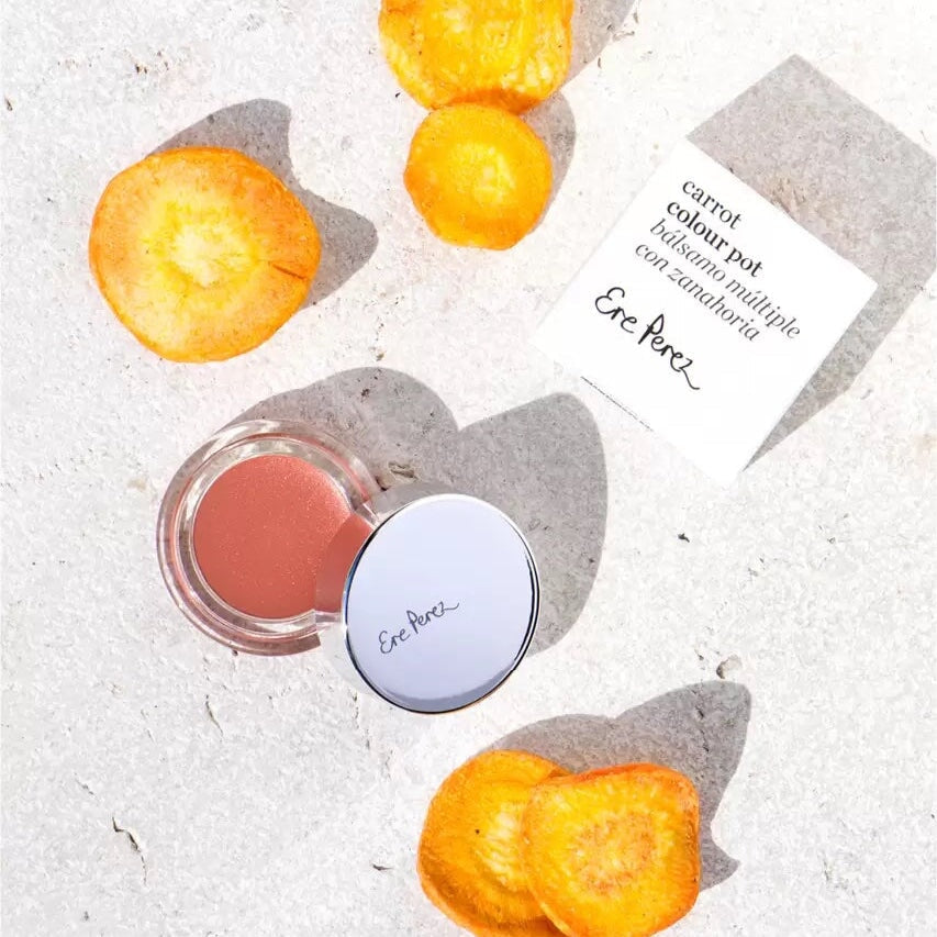  Ere Perez Carrot Colour Pot offener Tiegel und Verpackung liegen zwischen Karottenscheiben.