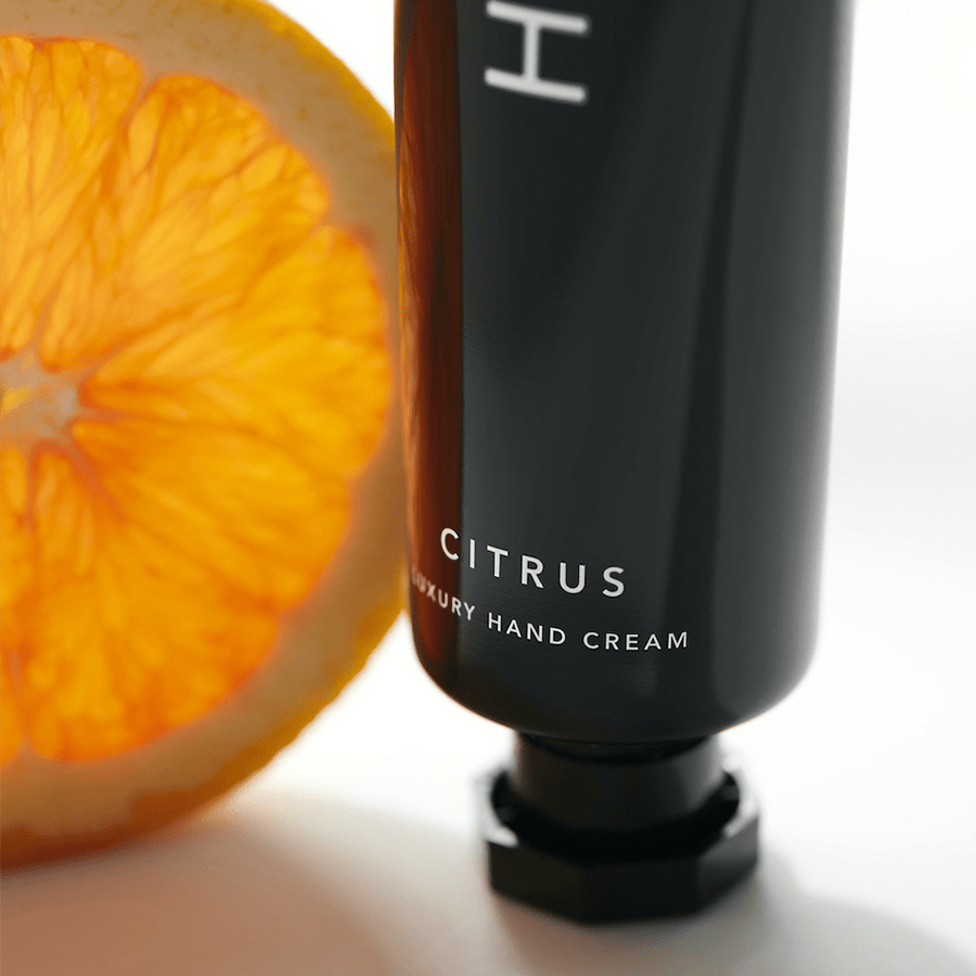 Nahaufnahme einer Tube Henné Organics Handcreme neben einer halben Orange. North Glow