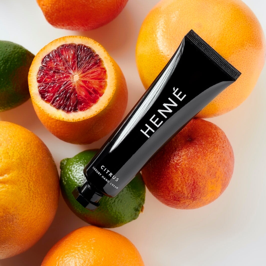 Schwarze Tube Henné Organics Handcreme Citrus liegt auf verschiedenen Zitrusfrüchten.