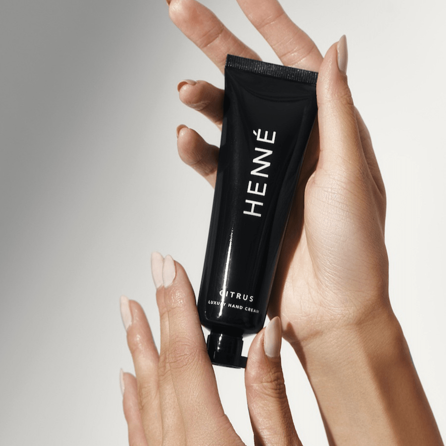 2 gepflegte Hände halten eine Henné Organics Tube Handcreme Citrus in die Luft. North Glow