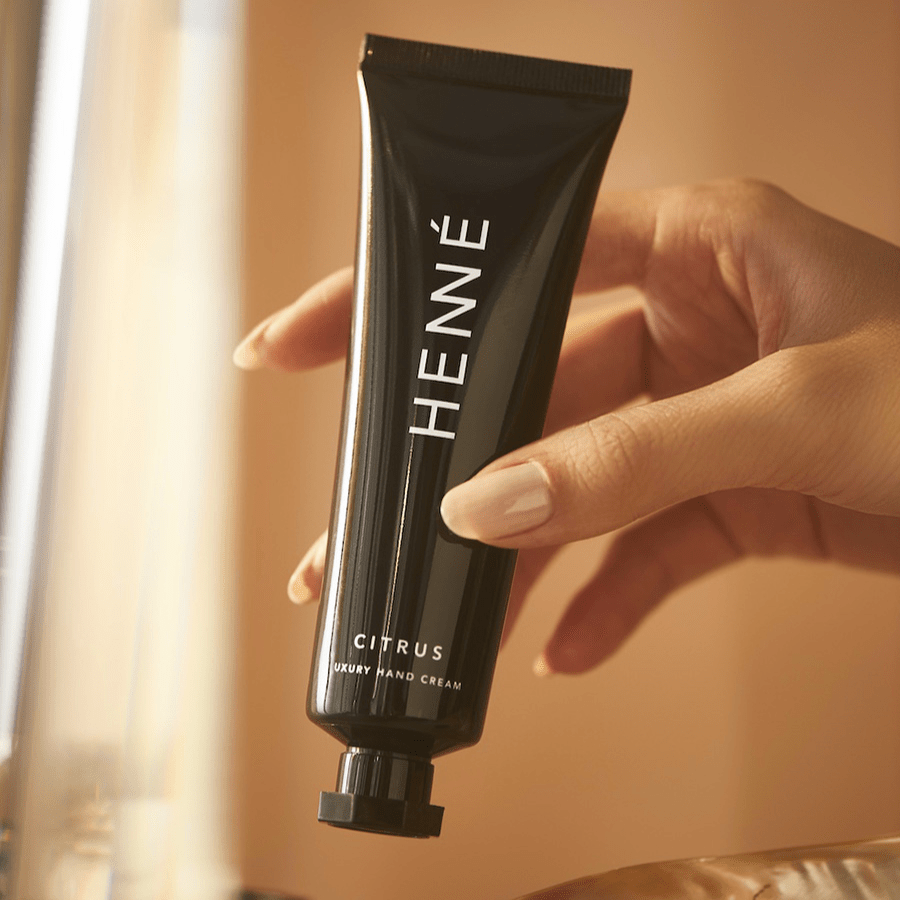 Eine Hand hält eine Tube Henné Organics Handcreme Citrus. North Glow