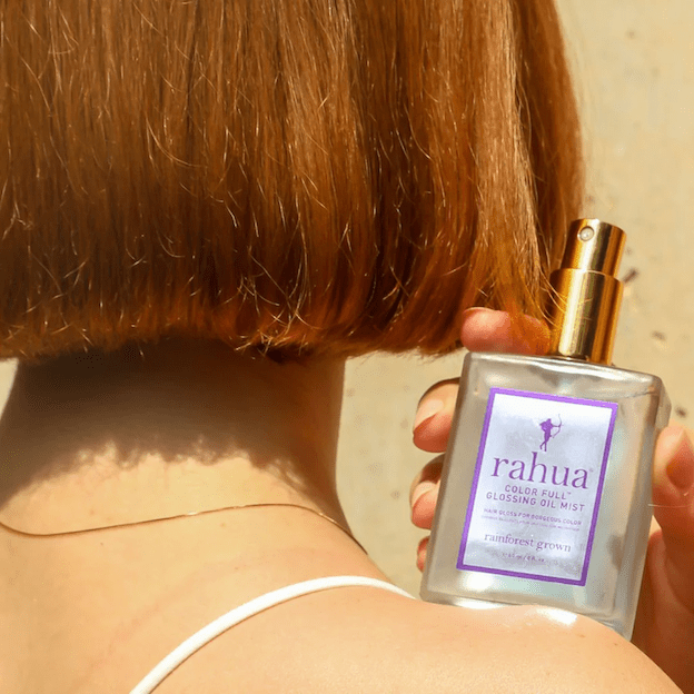 Nahaufnahme teils Kopf, teils Schulter einer rothaarigen Frau mit Bob Haarschnitt, hält in ihrer Hand auf der Schulter gestützt eine Rahua Color Full Glossing Oil Mist Flasche.