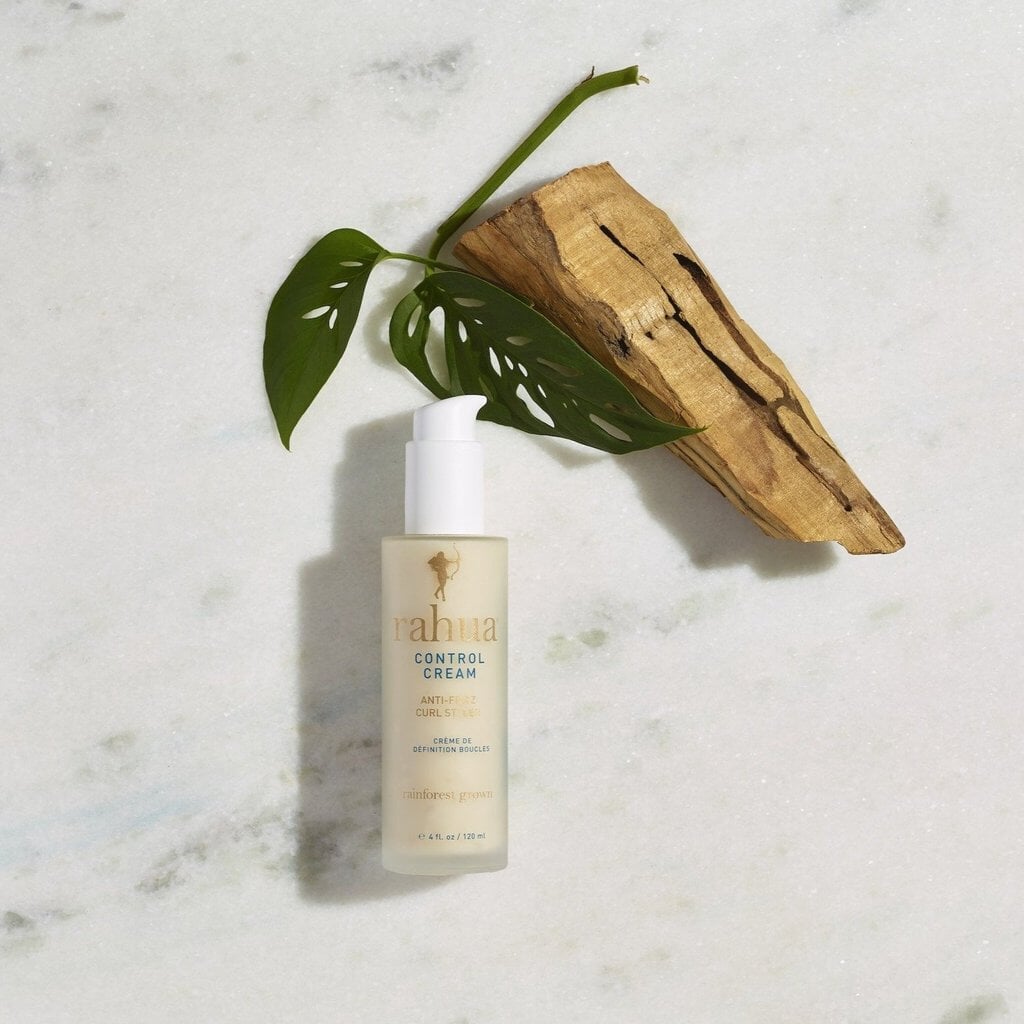 Rahua Control Cream Curl Styler Flasche auf heller Marmorplatte dekoriert mit Palmenblatt und einem Stück Holz.