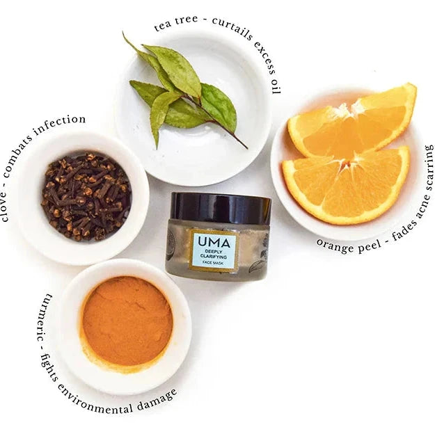 Schraubglas UMA Deeply Clarifying Face Mask umringt von Schüsselchen mit den Zutatan Nelken, Tea Tree Blättern, Orangenscheiben und Kurkumapulver.
