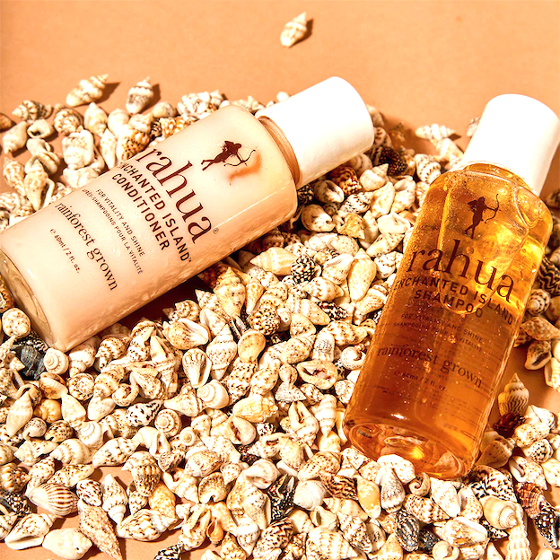 2 Flaschen in travel size Rahua Enchanted Island Shampoo und Conditioner auf einem Muschelbett.