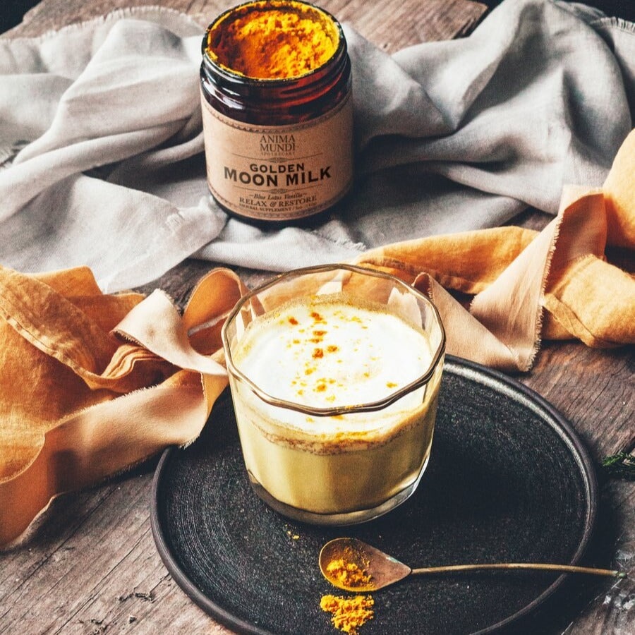 Golden Moon Milk im Glas auf dunklem Teller dekoriert mit Messinglöffel befüllt mit orangefarbenem Pulver.