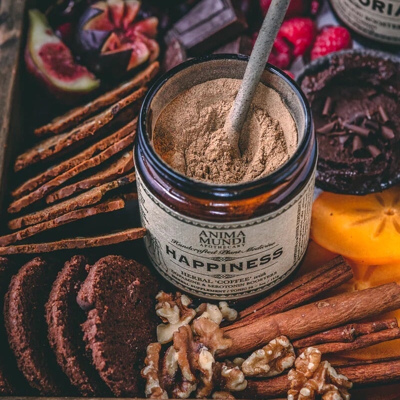 Anima Mundi Happiness Schraublas mit einem Löffel steht zwischen Keksen, Walnüssen, Zimtstangen und Schokolade.